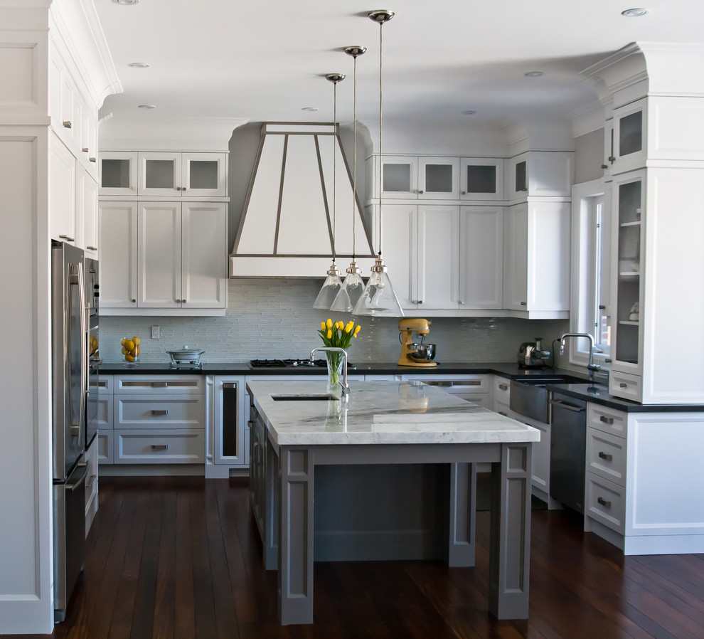 Design ideas for a large transitional u-shaped kitchen in Toronto with a farmhouse sink, recessed-panel cabinets, white cabinets, grey splashback, glass tile splashback, stainless steel appliances, medium hardwood floors and with island.