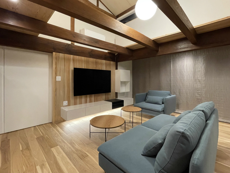 На фото: открытая гостиная комната среднего размера в восточном стиле с белыми стенами, полом из фанеры, деревянным потолком, телевизором на стене и деревянными стенами