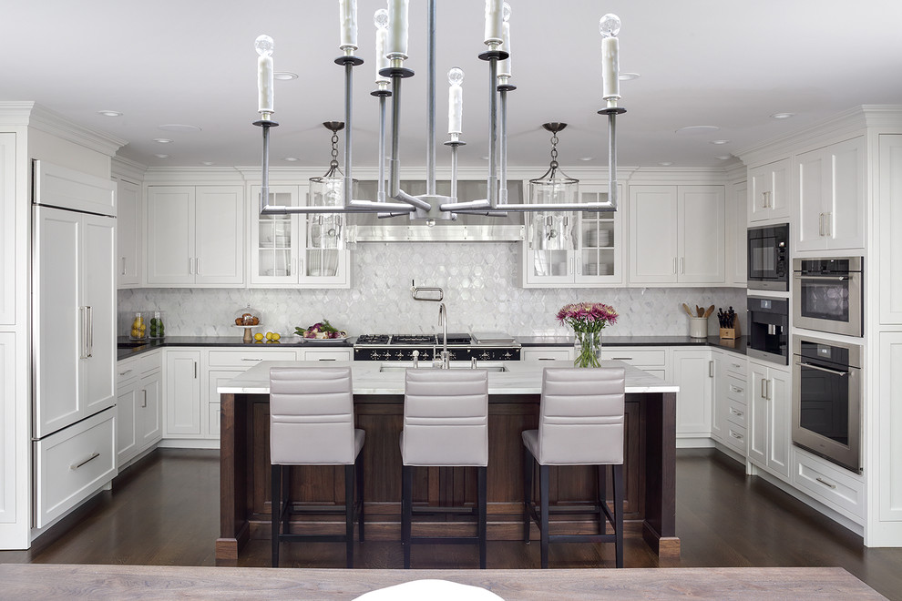 Kitchen - Large family kitchen with a center island seating. White cabinetry set off against a dark hardwood floor. Island countertop in white marble contrasts with the black countertops along the back wall.