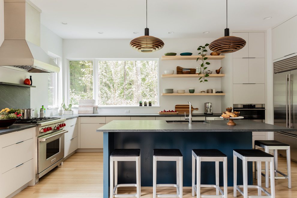 Photo of a beach style l-shaped kitchen in Boston with an undermount sink, flat-panel cabinets, grey splashback, stainless steel appliances, light hardwood floors, with island, beige floor, grey benchtop and beige cabinets.
