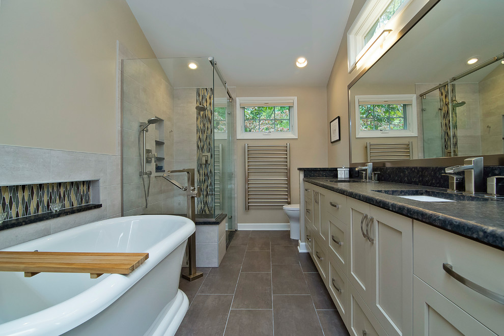 Design ideas for a mid-sized contemporary master bathroom in Raleigh with shaker cabinets, grey cabinets, a freestanding tub, a curbless shower, a two-piece toilet, beige tile, porcelain tile, beige walls, porcelain floors, an undermount sink, granite benchtops, brown floor, a hinged shower door and black benchtops.