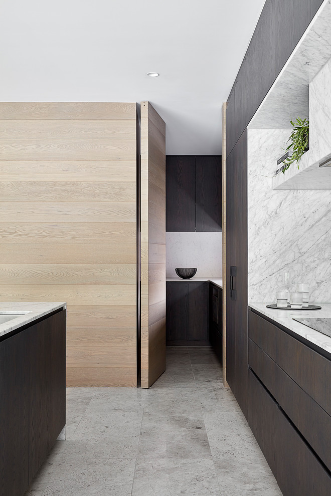 Large contemporary galley kitchen pantry in Melbourne with a drop-in sink, dark wood cabinets, marble benchtops, grey splashback, marble splashback, black appliances, limestone floors, with island, grey floor and grey benchtop.