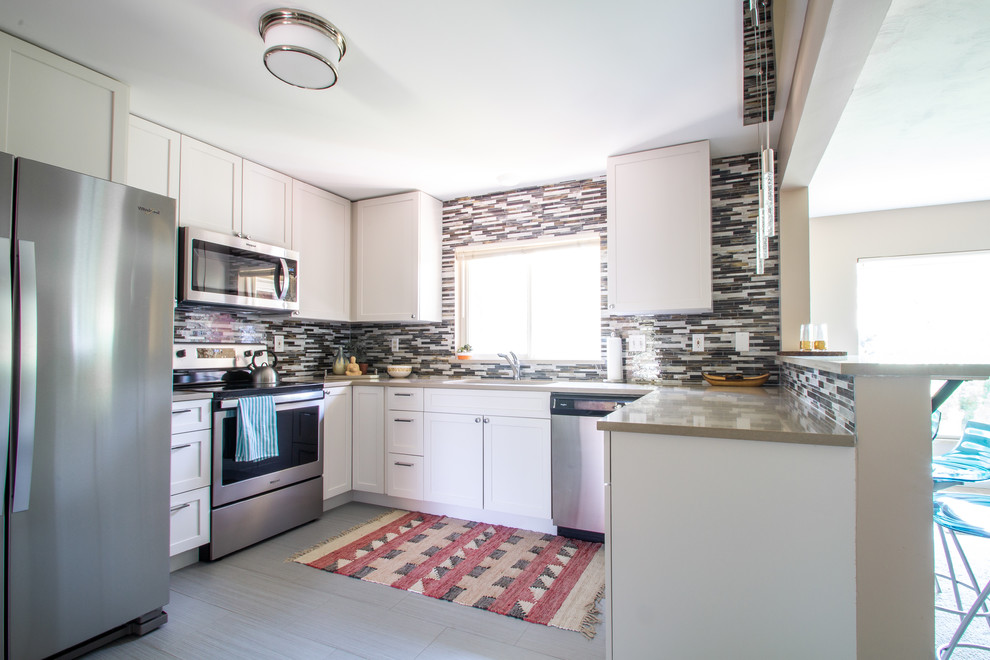This is an example of a mid-sized midcentury u-shaped eat-in kitchen in Denver with a drop-in sink, shaker cabinets, white cabinets, quartz benchtops, multi-coloured splashback, glass tile splashback, stainless steel appliances, ceramic floors, with island, grey floor and grey benchtop.
