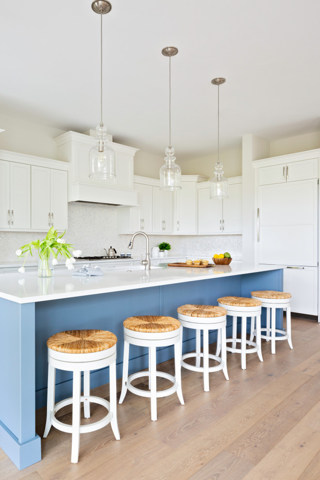 Inspiration for a large beach style l-shaped open plan kitchen in Tampa with an undermount sink, shaker cabinets, white cabinets, white splashback, panelled appliances, light hardwood floors, with island, beige floor and white benchtop.