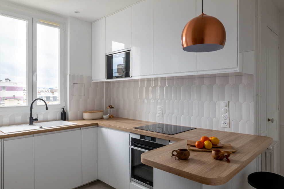 This is an example of a mid-sized scandinavian u-shaped eat-in kitchen in Paris with white cabinets, white splashback, black appliances, light hardwood floors, with island and brown benchtop.