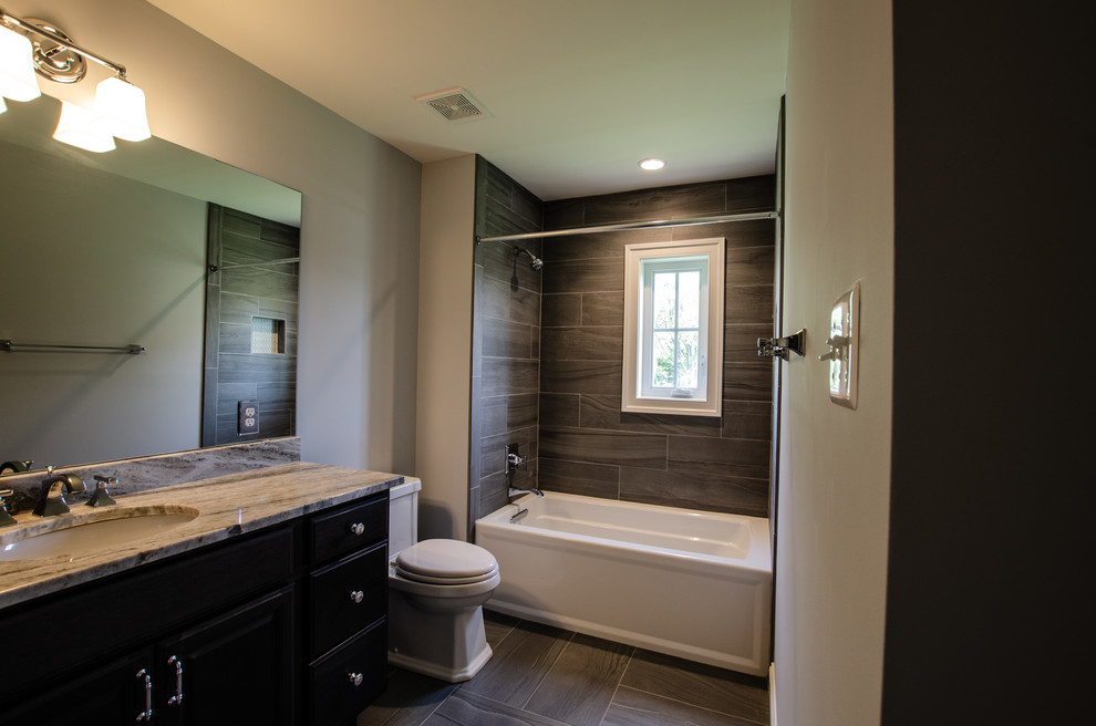 Design ideas for a mid-sized transitional 3/4 bathroom in Baltimore with recessed-panel cabinets, black cabinets, an alcove tub, a shower/bathtub combo, a two-piece toilet, beige tile, porcelain tile, grey walls, laminate floors, an undermount sink, granite benchtops, brown floor, a shower curtain and beige benchtops.