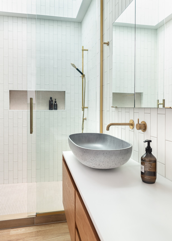 This is an example of a contemporary bathroom in Auckland with flat-panel cabinets, medium wood cabinets, an alcove shower, white tile, medium hardwood floors, a vessel sink, brown floor, an open shower, white benchtops, a niche, a single vanity and a floating vanity.
