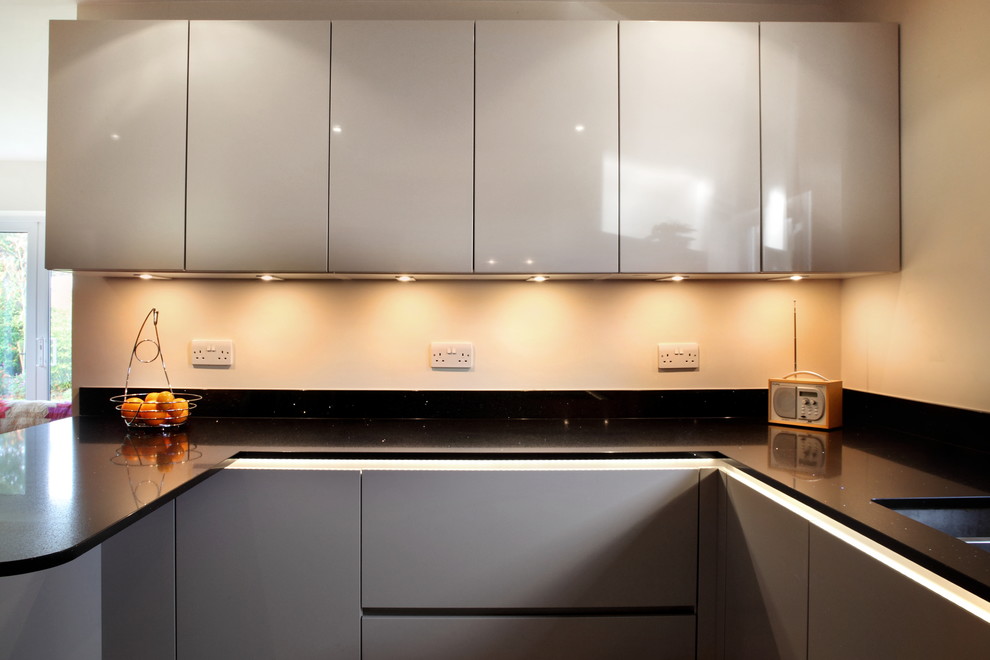 Mid-sized contemporary u-shaped eat-in kitchen in Buckinghamshire with flat-panel cabinets, grey cabinets, quartzite benchtops, orange splashback, glass sheet splashback, stainless steel appliances, terra-cotta floors, a peninsula and an undermount sink.