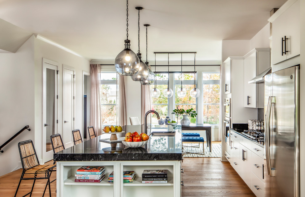 Eat-in kitchen - transitional galley medium tone wood floor and brown floor eat-in kitchen idea in Denver with an undermount sink, flat-panel cabinets, white cabinets, stainless steel appliances, an island and black countertops