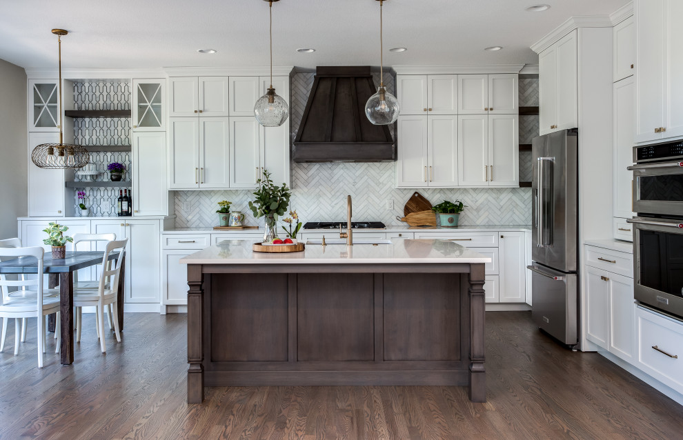 Inspiration for a large transitional l-shaped open plan kitchen in Denver with an undermount sink, shaker cabinets, white cabinets, quartz benchtops, beige splashback, marble splashback, stainless steel appliances, medium hardwood floors, with island, brown floor and white benchtop.