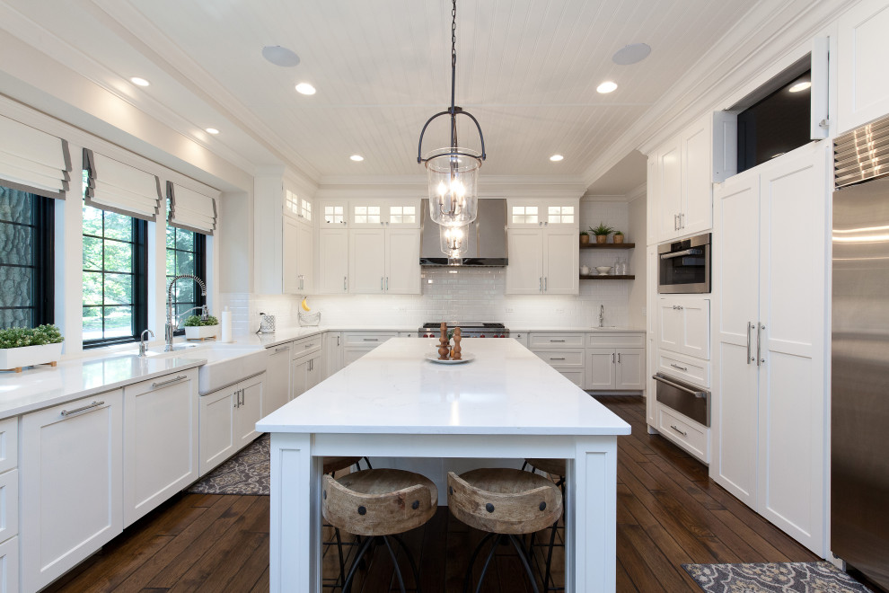 This is an example of a modern kitchen in Chicago with a farmhouse sink, quartzite benchtops, white splashback, subway tile splashback, stainless steel appliances, dark hardwood floors, with island, brown floor, white benchtop and timber.