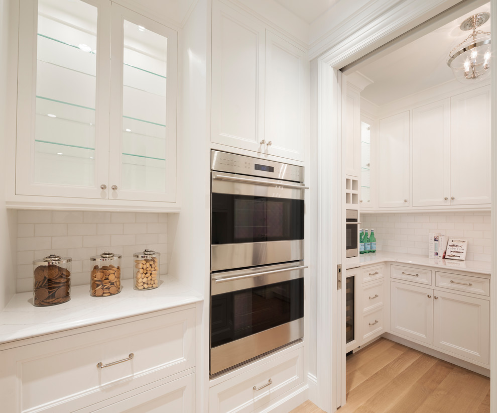 Inspiration for a large transitional l-shaped eat-in kitchen in Minneapolis with a farmhouse sink, recessed-panel cabinets, white cabinets, quartzite benchtops, white splashback, subway tile splashback, panelled appliances, light hardwood floors and with island.
