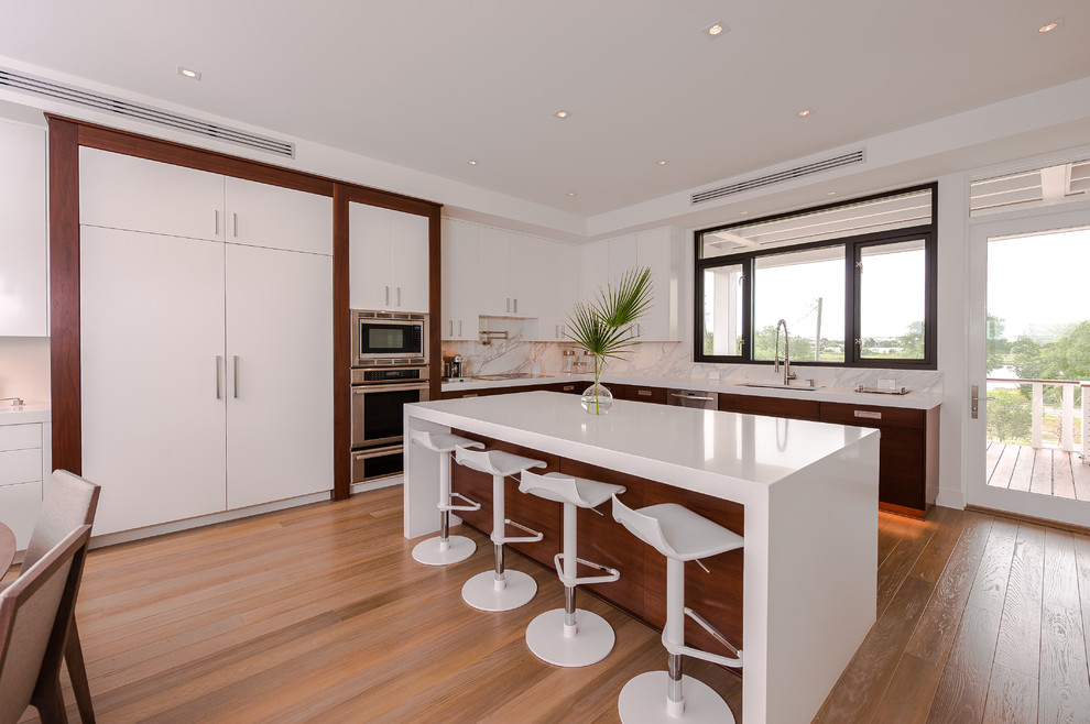 Enclosed kitchen - large l-shaped light wood floor enclosed kitchen idea in Orange County with an undermount sink, flat-panel cabinets, white cabinets, solid surface countertops, multicolored backsplash, stone slab backsplash, stainless steel appliances and an island