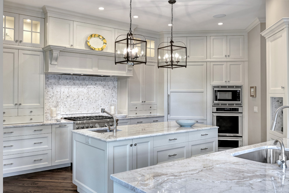 Large traditional u-shaped open plan kitchen in Charleston with an undermount sink, recessed-panel cabinets, white cabinets, marble benchtops, grey splashback, mosaic tile splashback, stainless steel appliances, medium hardwood floors, multiple islands, brown floor and white benchtop.