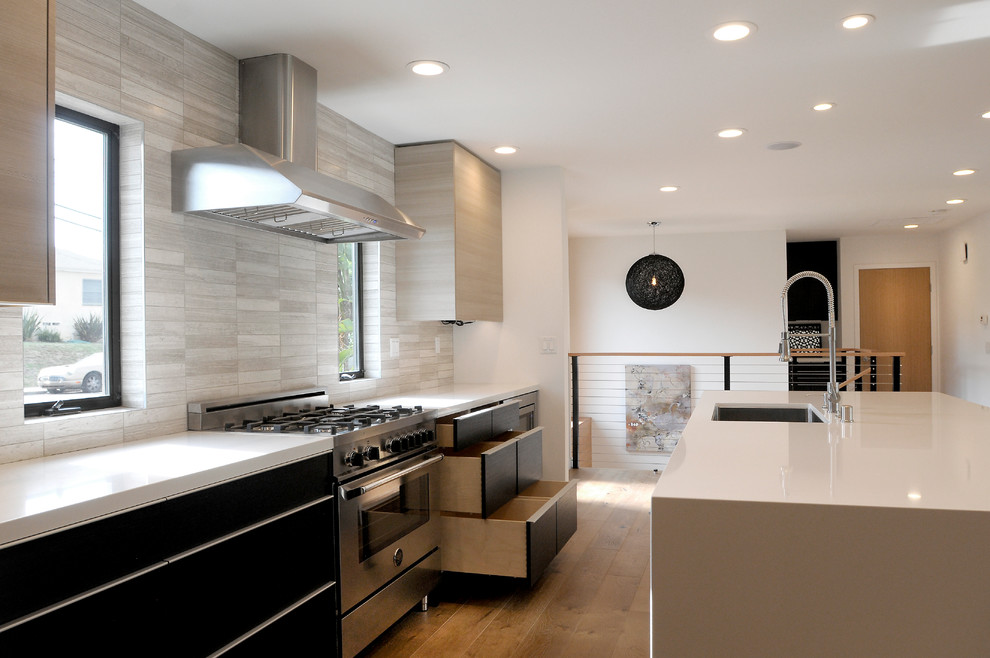 This is an example of a large modern l-shaped open plan kitchen in San Diego with a single-bowl sink, flat-panel cabinets, black cabinets, quartz benchtops, grey splashback, subway tile splashback, stainless steel appliances, medium hardwood floors and with island.