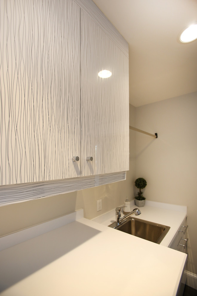 Inspiration for a large beach style single-wall dedicated laundry room in Philadelphia with a drop-in sink, flat-panel cabinets, white cabinets, solid surface benchtops, white walls, vinyl floors and a side-by-side washer and dryer.