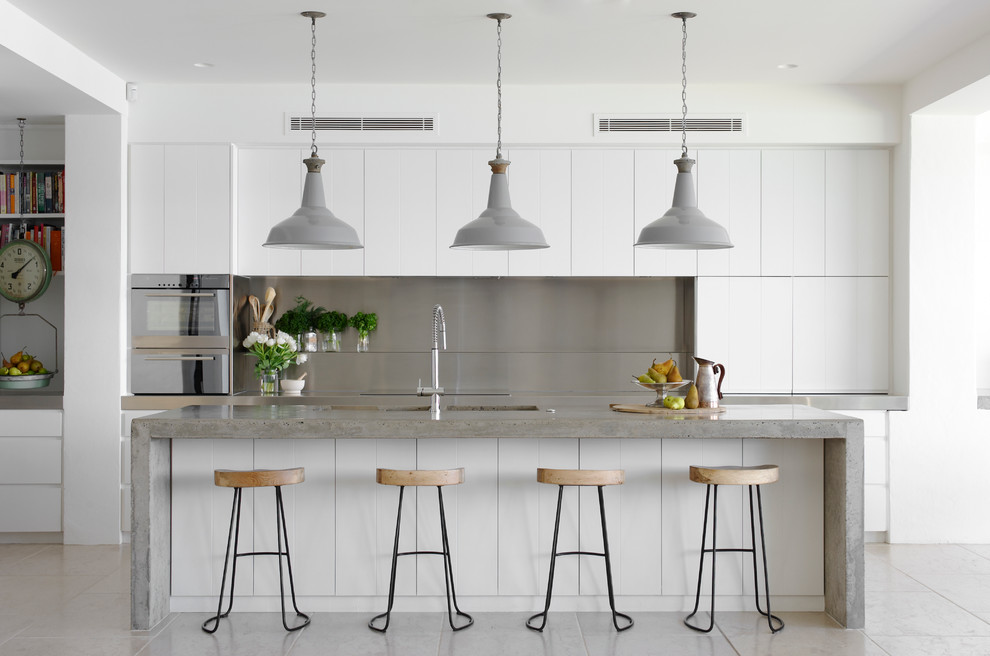 Mid-sized beach style galley eat-in kitchen in Sydney with an undermount sink, flat-panel cabinets, white cabinets, concrete benchtops, metal splashback, stainless steel appliances, with island and grey splashback.