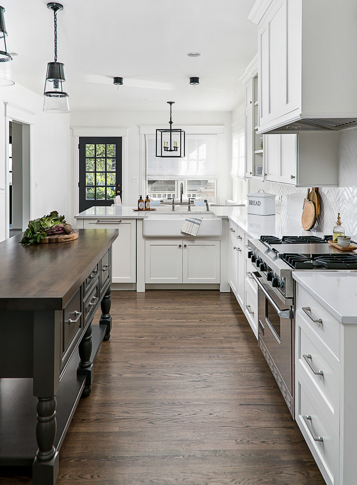Inspiration for a mid-sized traditional u-shaped eat-in kitchen in Chicago with a farmhouse sink, shaker cabinets, white cabinets, quartz benchtops, white splashback, porcelain splashback, stainless steel appliances, dark hardwood floors, a peninsula and brown floor.