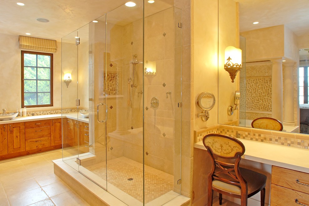 Large mediterranean master bathroom in San Diego with shaker cabinets, medium wood cabinets, a drop-in tub, an open shower, beige tile, beige walls, limestone floors, a vessel sink, limestone benchtops, limestone, a one-piece toilet, beige floor and a hinged shower door.