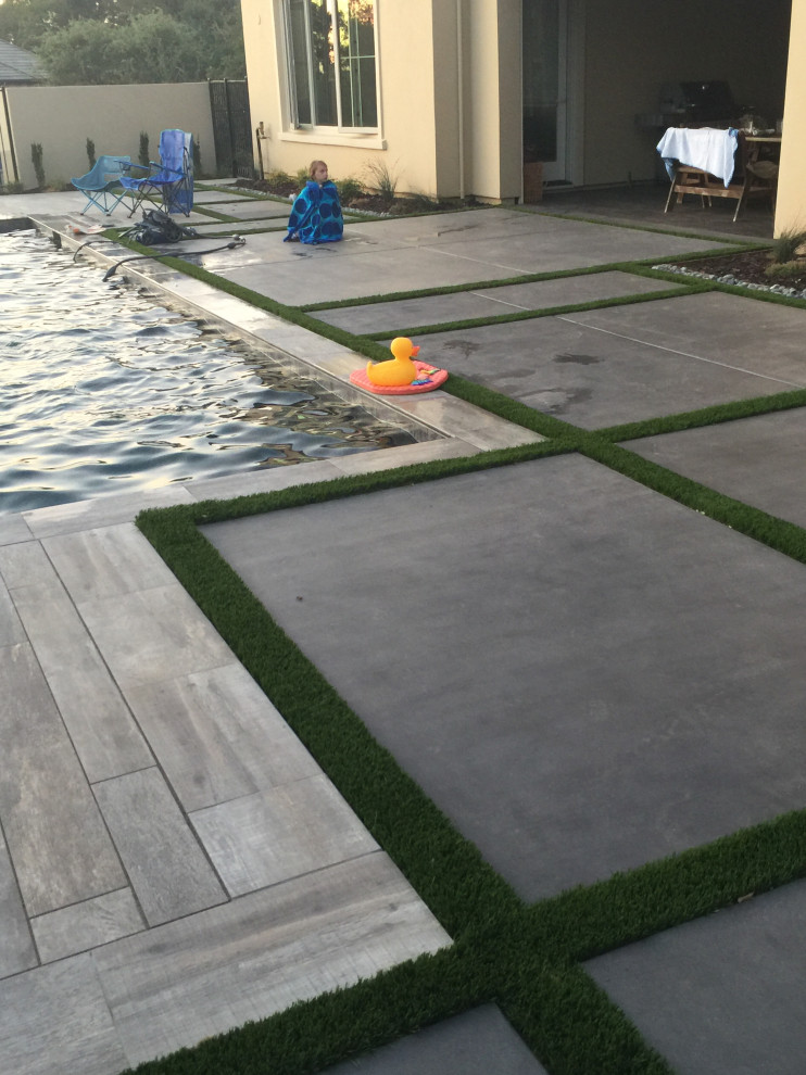 Cette photo montre un grand piscine avec aménagement paysager arrière chic rectangle avec une dalle de béton.