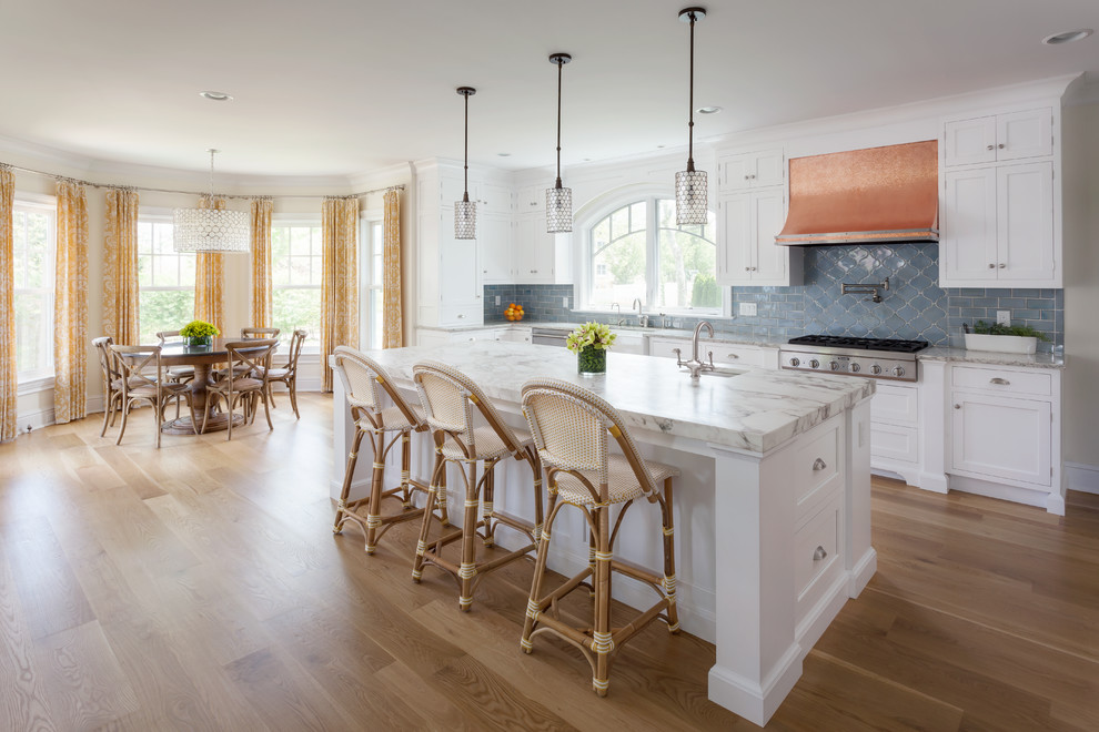 This is an example of a beach style galley eat-in kitchen in Baltimore with a farmhouse sink, white cabinets, marble benchtops, blue splashback, ceramic splashback, stainless steel appliances, medium hardwood floors, with island and shaker cabinets.