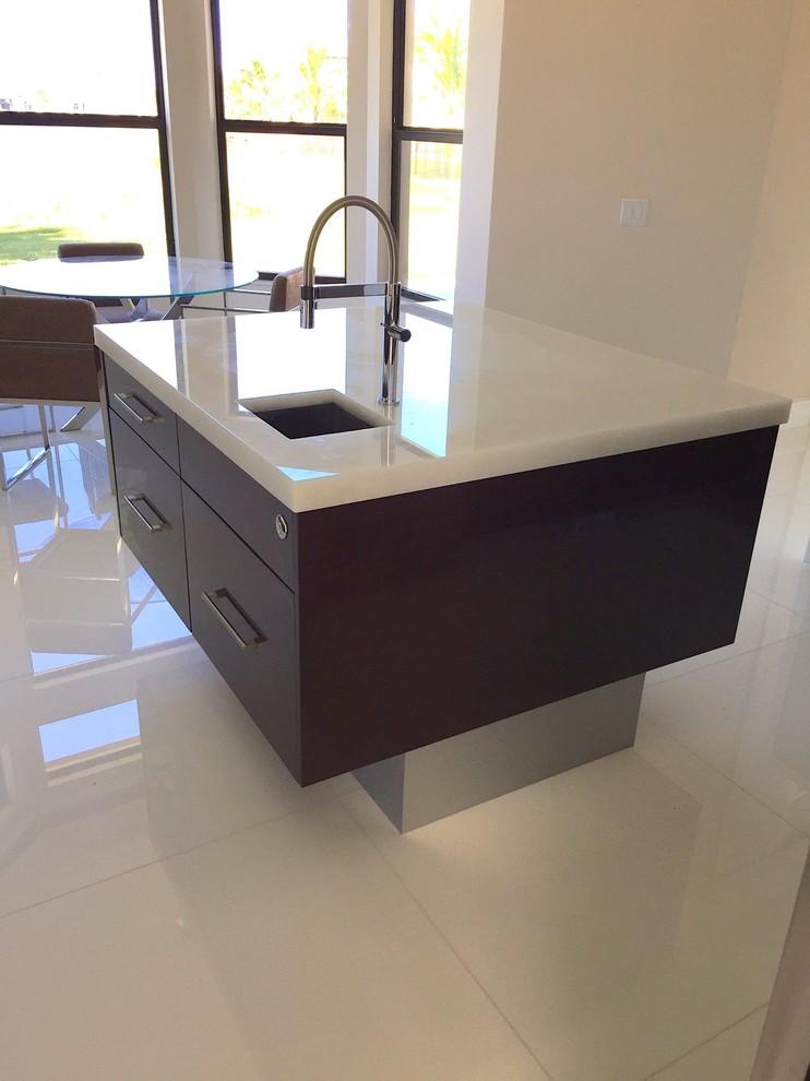 This is an example of a large contemporary u-shaped open plan kitchen in Miami with a single-bowl sink, flat-panel cabinets, dark wood cabinets, recycled glass benchtops, white splashback, glass sheet splashback, stainless steel appliances, porcelain floors, with island and white floor.