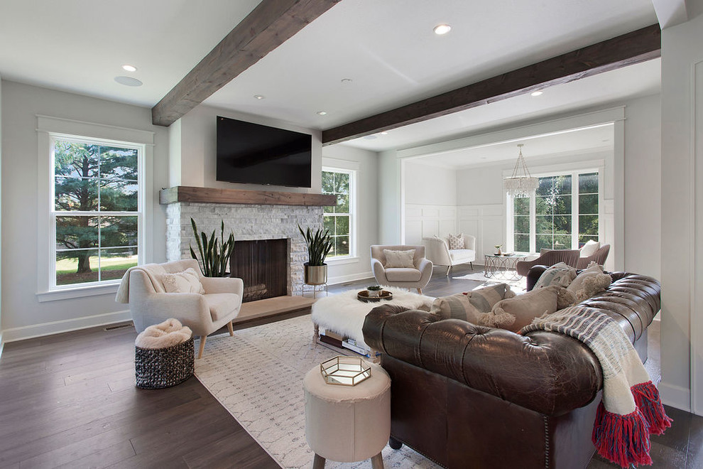 Photo of a large country open concept living room in Kansas City with grey walls, dark hardwood floors, a wood stove, a stone fireplace surround, a wall-mounted tv and brown floor.