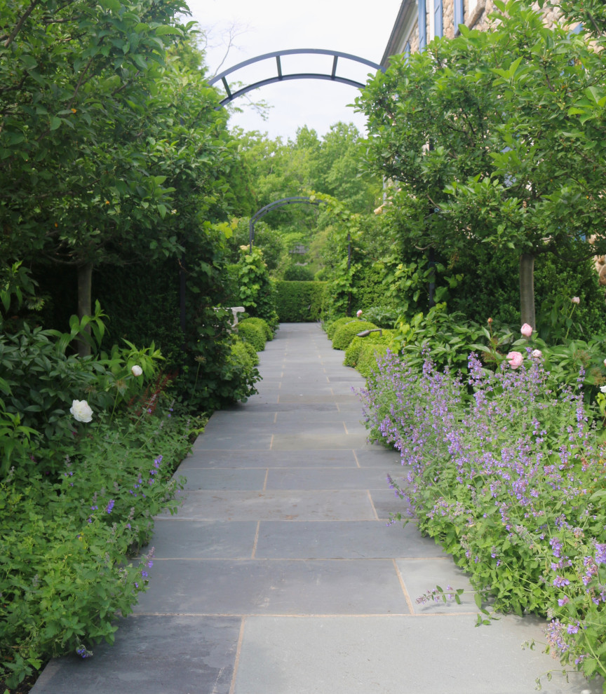 На фото: большой летний регулярный сад на боковом дворе в классическом стиле с дорожками, полуденной тенью и покрытием из каменной брусчатки с