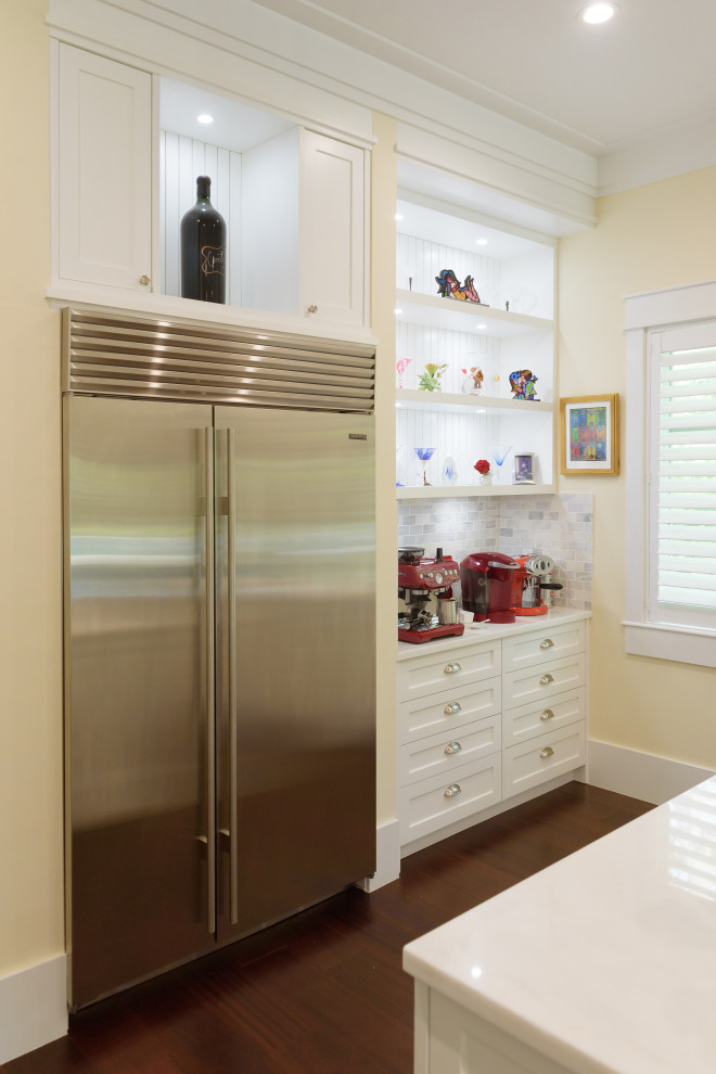 Bild på ett stort lantligt vit vitt kök, med en undermonterad diskho, skåp i shakerstil, vita skåp, bänkskiva i kvarts, grått stänkskydd, stänkskydd i porslinskakel, rostfria vitvaror, mellanmörkt trägolv, en köksö och brunt golv