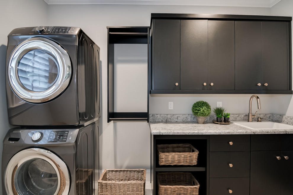 Small transitional single-wall dedicated laundry room in Other with an utility sink, flat-panel cabinets, black cabinets, laminate benchtops, grey walls, ceramic floors, a stacked washer and dryer and multi-coloured benchtop.