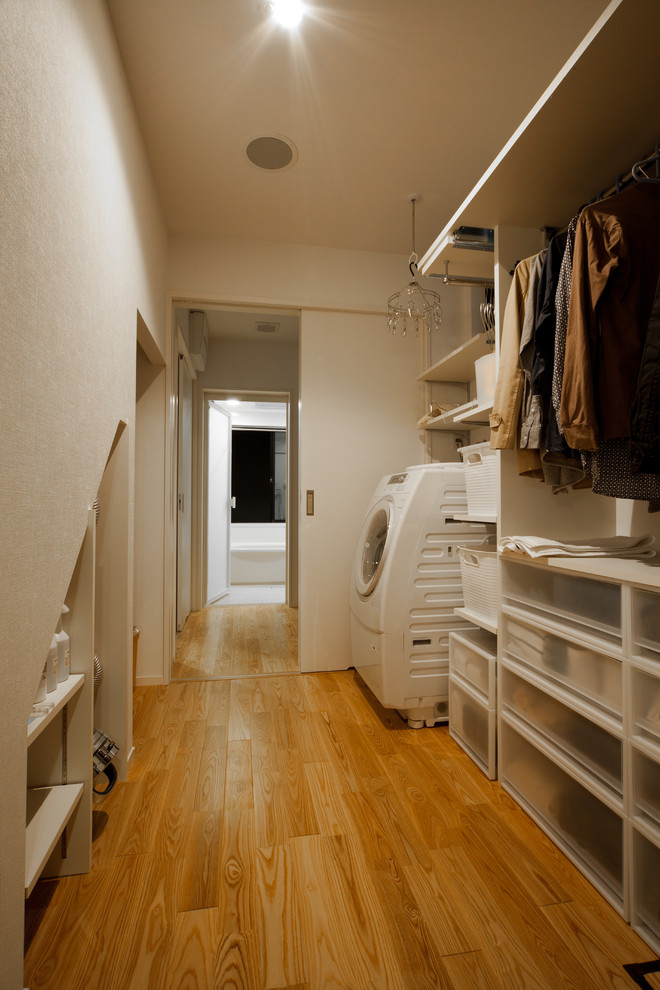 Inspiration for a contemporary laundry room in Kyoto with open cabinets, white cabinets, white walls, medium hardwood floors, brown floor and an integrated washer and dryer.