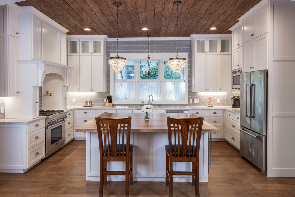 This is an example of a large arts and crafts u-shaped eat-in kitchen in Austin with a farmhouse sink, shaker cabinets, white cabinets, granite benchtops, grey splashback, subway tile splashback, stainless steel appliances, medium hardwood floors, with island and multi-coloured benchtop.
