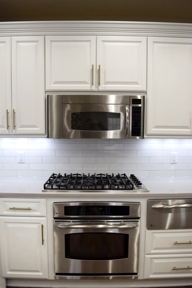 Inspiration for a transitional dark wood floor eat-in kitchen remodel in Milwaukee with an undermount sink, raised-panel cabinets, white cabinets, white backsplash, stainless steel appliances and gray countertops