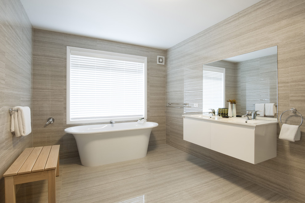Mid-sized contemporary master bathroom in Auckland with white cabinets, a freestanding tub, a wall-mount toilet, beige tile, ceramic tile, beige walls, ceramic floors, an integrated sink and engineered quartz benchtops.