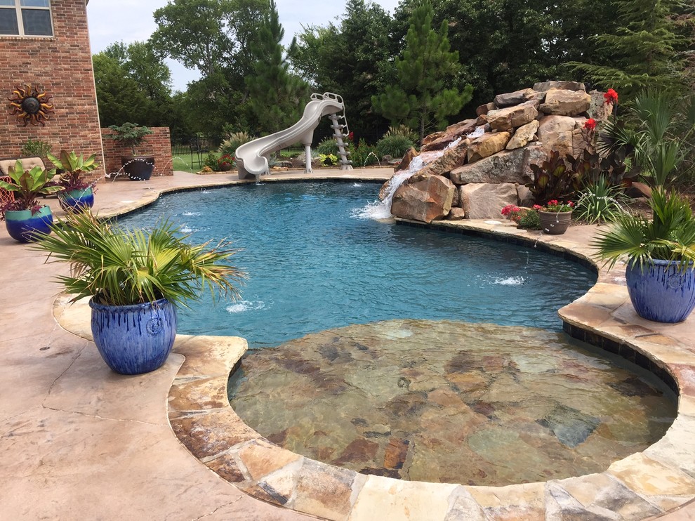 Photo of a large tropical backyard custom-shaped natural pool in Oklahoma City with a water slide and stamped concrete.