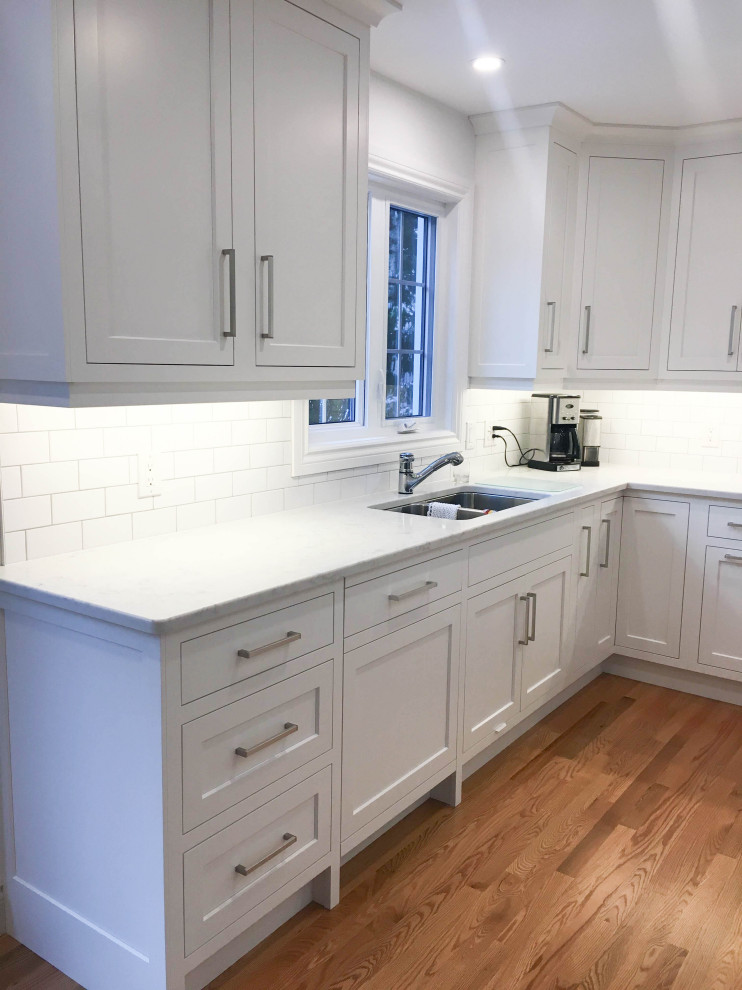 Large transitional u-shaped light wood floor and beige floor eat-in kitchen photo with a double-bowl sink, shaker cabinets, white cabinets, quartzite countertops, white backsplash, subway tile backsplash, stainless steel appliances, an island and white countertops