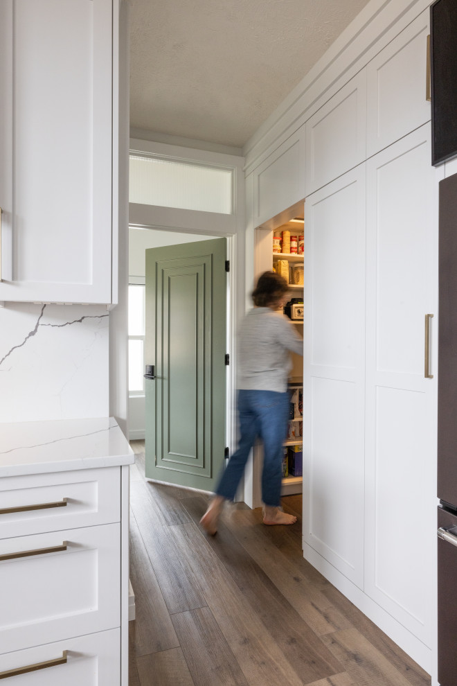 Mid-sized transitional vinyl floor and brown floor eat-in kitchen photo in Omaha with an undermount sink, shaker cabinets, white cabinets, quartz countertops, white backsplash, stone slab backsplash, stainless steel appliances, an island and black countertops