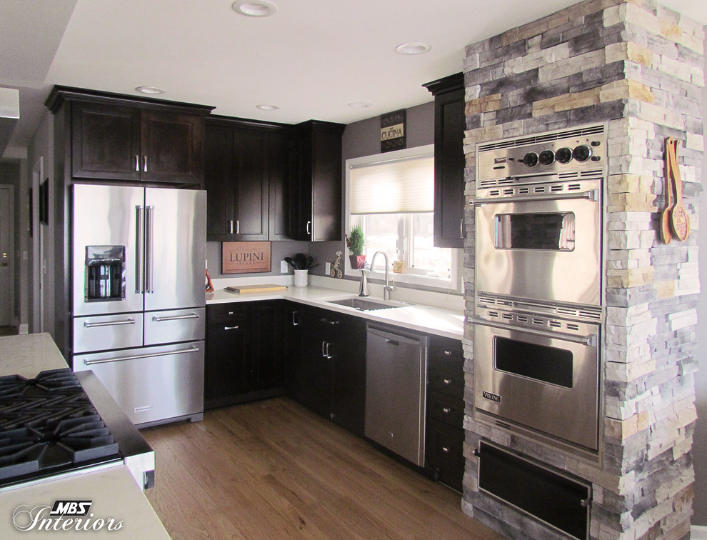 Eat-in kitchen - large transitional l-shaped light wood floor eat-in kitchen idea with an undermount sink, recessed-panel cabinets, dark wood cabinets, quartz countertops, stainless steel appliances and an island