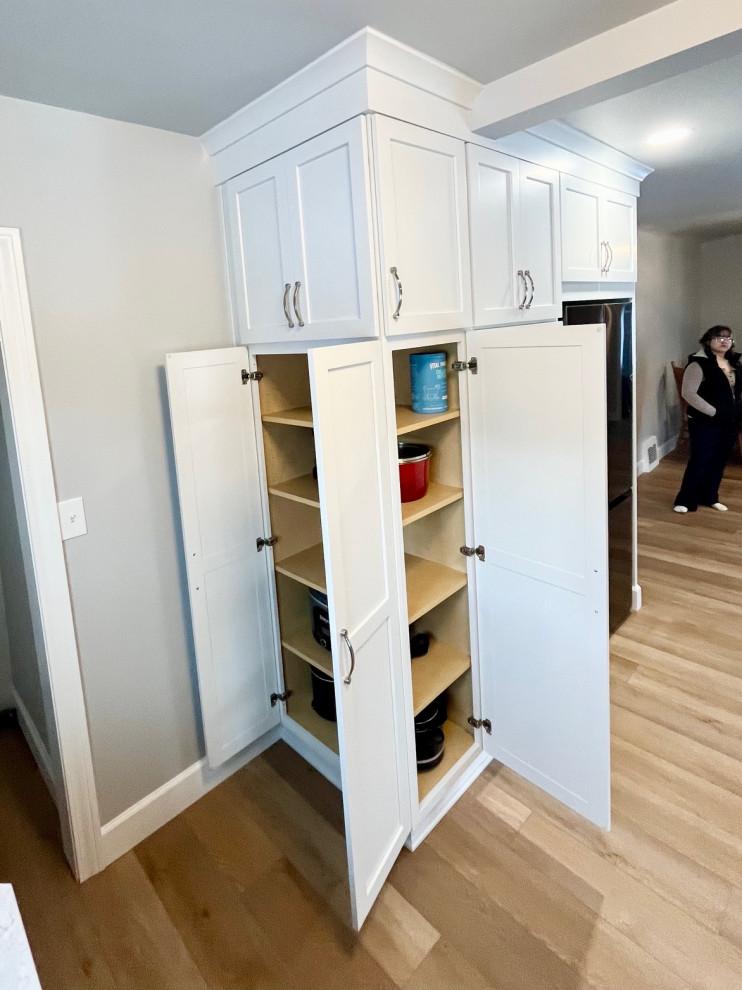 Example of a mid-sized transitional u-shaped vinyl floor and brown floor eat-in kitchen design with an undermount sink, shaker cabinets, white cabinets, quartz countertops, white backsplash, ceramic backsplash, stainless steel appliances, no island and white countertops
