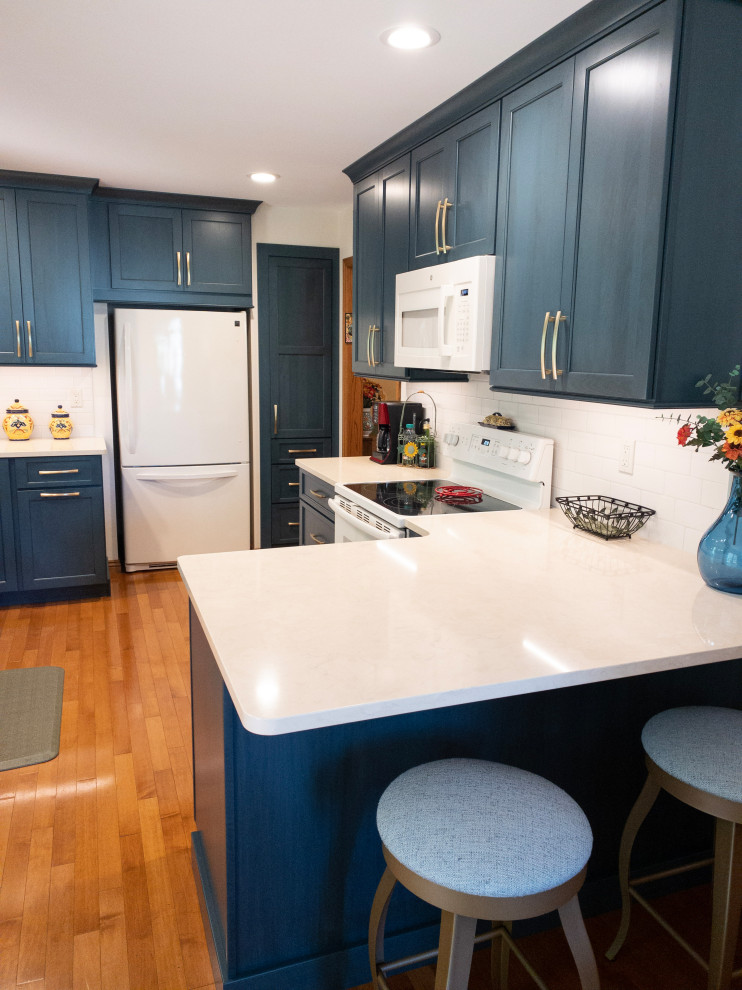 Example of a mid-sized transitional galley light wood floor enclosed kitchen design with an undermount sink, flat-panel cabinets, blue cabinets, quartz countertops, white backsplash, subway tile backsplash, white appliances, a peninsula and white countertops