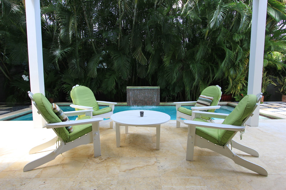 This is an example of a mid-sized tropical backyard patio in Miami with a water feature and natural stone pavers.