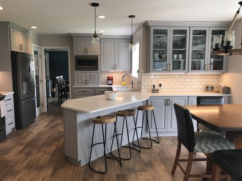 This is an example of a mid-sized transitional u-shaped separate kitchen in Other with an undermount sink, raised-panel cabinets, grey cabinets, quartz benchtops, white splashback, ceramic splashback, vinyl floors, a peninsula, brown floor and white benchtop.