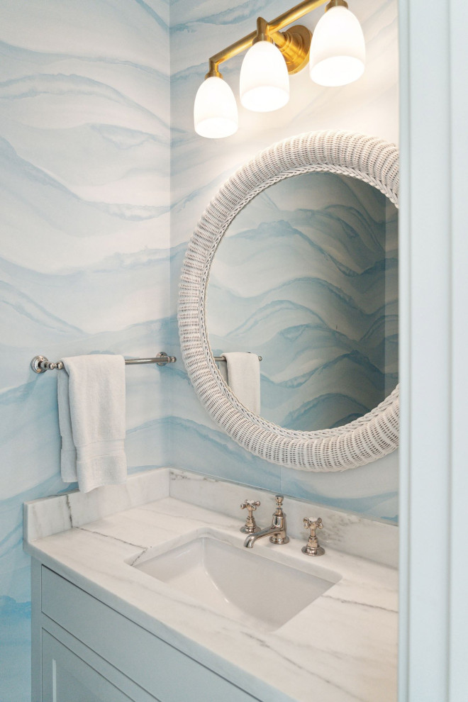 Design ideas for a beach style powder room in Charleston with blue cabinets, blue walls, an undermount sink, marble benchtops, white benchtops, a freestanding vanity, shaker cabinets and wallpaper.