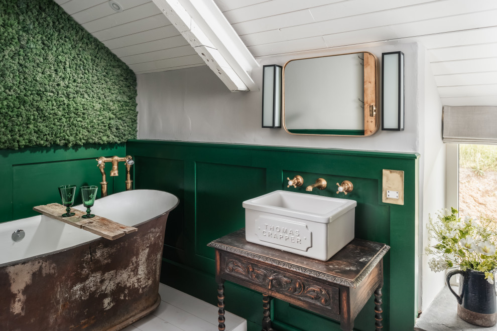 Photo of a small country master bathroom in Other with dark wood cabinets, a freestanding tub, a wall-mount toilet, green tile, green walls, painted wood floors, wood benchtops, white floor, brown benchtops, a single vanity, a freestanding vanity, panelled walls, a curbless shower, a trough sink and a hinged shower door.