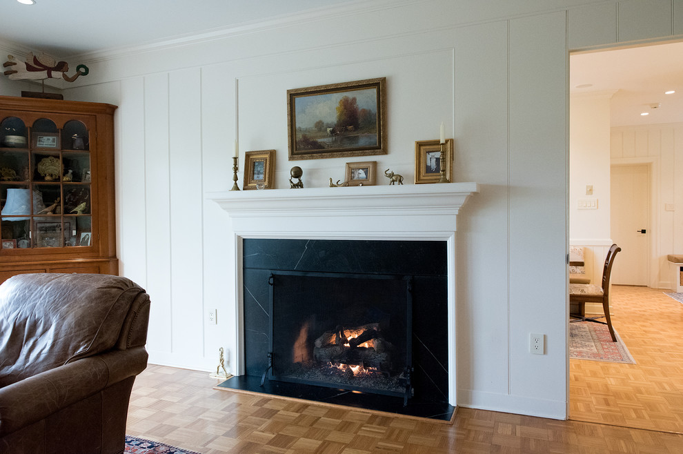 This is an example of a mid-sized traditional enclosed living room in Philadelphia with a library, white walls, light hardwood floors, a standard fireplace, a stone fireplace surround and brown floor.
