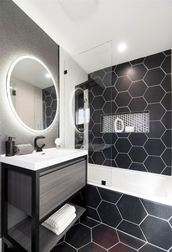 Пример оригинального дизайна: ванная комната в стиле ретро с плоскими фасадами, серыми фасадами, ванной в нише, душем над ванной, унитазом-моноблоком, черно-белой плиткой, керамической плиткой, черными стенами, полом из керамической плитки, монолитной раковиной, столешницей из искусственного кварца, черным полом, душем с распашными дверями, черной столешницей, нишей, тумбой под одну раковину и подвесной тумбой