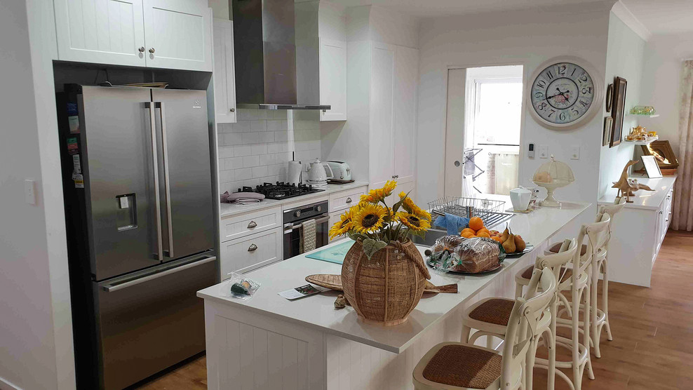 Inspiration for a mid-sized contemporary single-wall eat-in kitchen in Sunshine Coast with a drop-in sink, beaded inset cabinets, yellow cabinets, quartz benchtops, white splashback, subway tile splashback, stainless steel appliances, medium hardwood floors, with island, brown floor and white benchtop.
