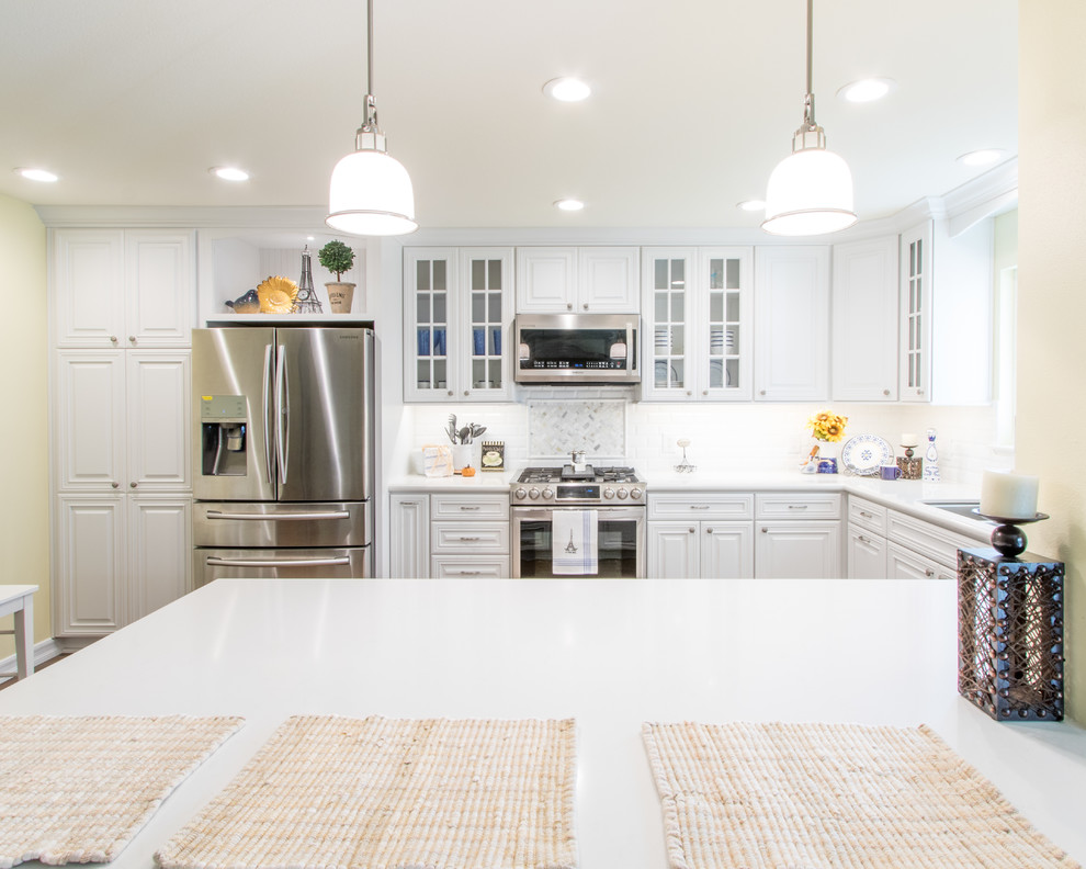 This is an example of a mid-sized traditional u-shaped eat-in kitchen in Orange County with an undermount sink, raised-panel cabinets, white cabinets, quartz benchtops, white splashback, ceramic splashback, stainless steel appliances and porcelain floors.