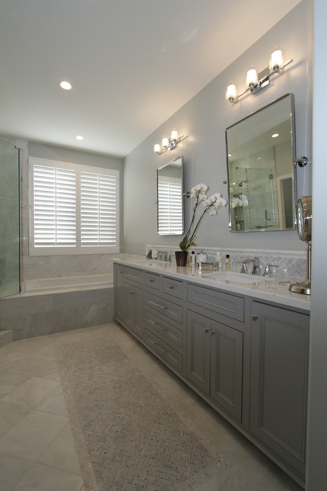 Design ideas for a mid-sized transitional master bathroom in Orange County with beaded inset cabinets, grey cabinets, a one-piece toilet, white tile, porcelain tile, grey walls, porcelain floors, an undermount sink, engineered quartz benchtops, grey floor, a sliding shower screen, a drop-in tub and a corner shower.