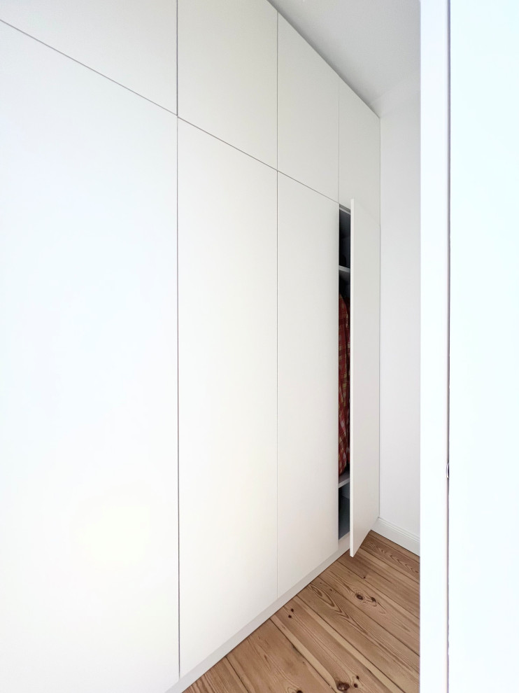 Cette image montre une petite buanderie design en L avec un placard, un placard à porte plane, des portes de placard blanches, un mur blanc, parquet clair et un sol marron.